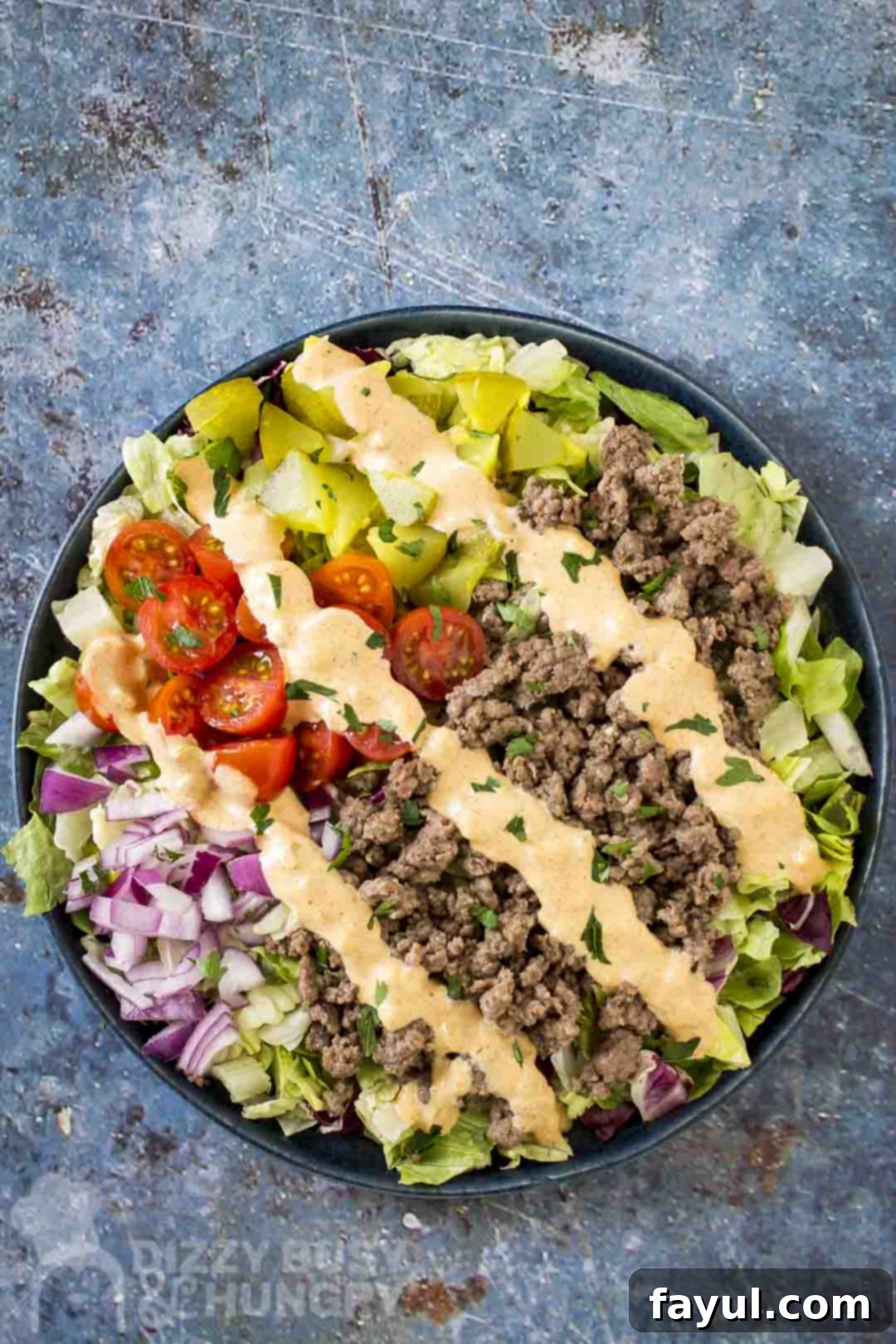 Overhead shot of big mac bowl drizzled with sauce and garnished with herbs in a blue bowl.