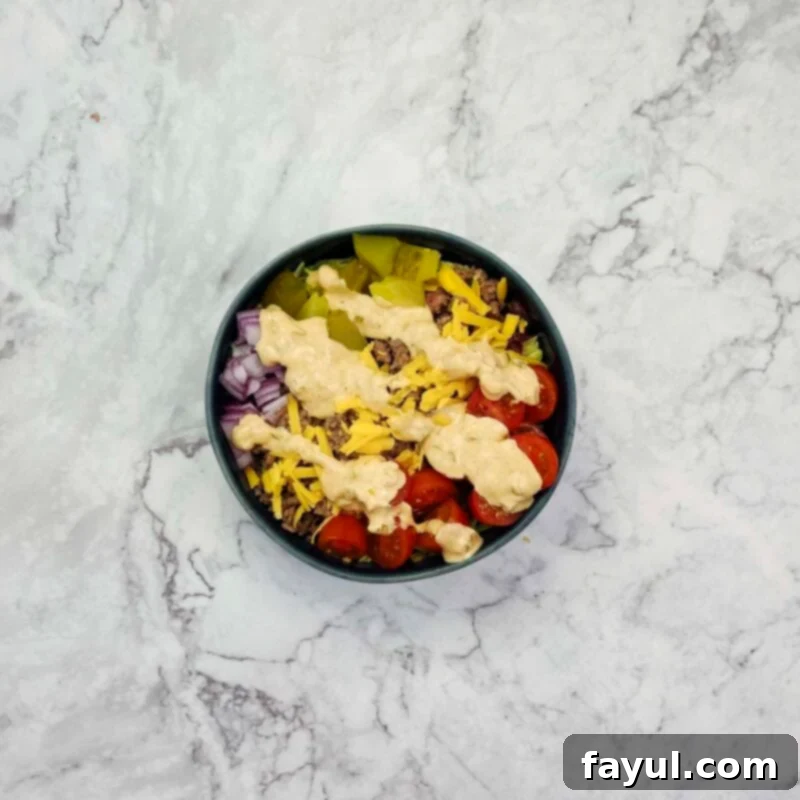 Overhead view of process shot 4 - top with cooked beef, shredded cheese, diced pickles, diced onions, and cherry tomatoes. Drizzle the big mac sauce over the bowls and serve.