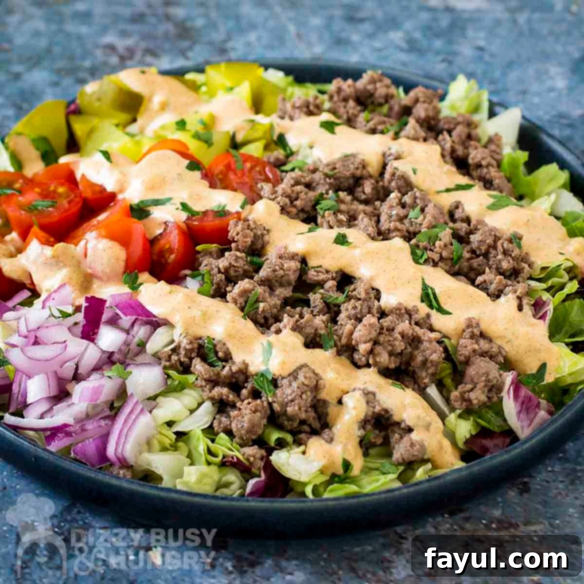 Side shot of big mac bowl drizzled with sauce and garnished with herbs in a blue bowl.