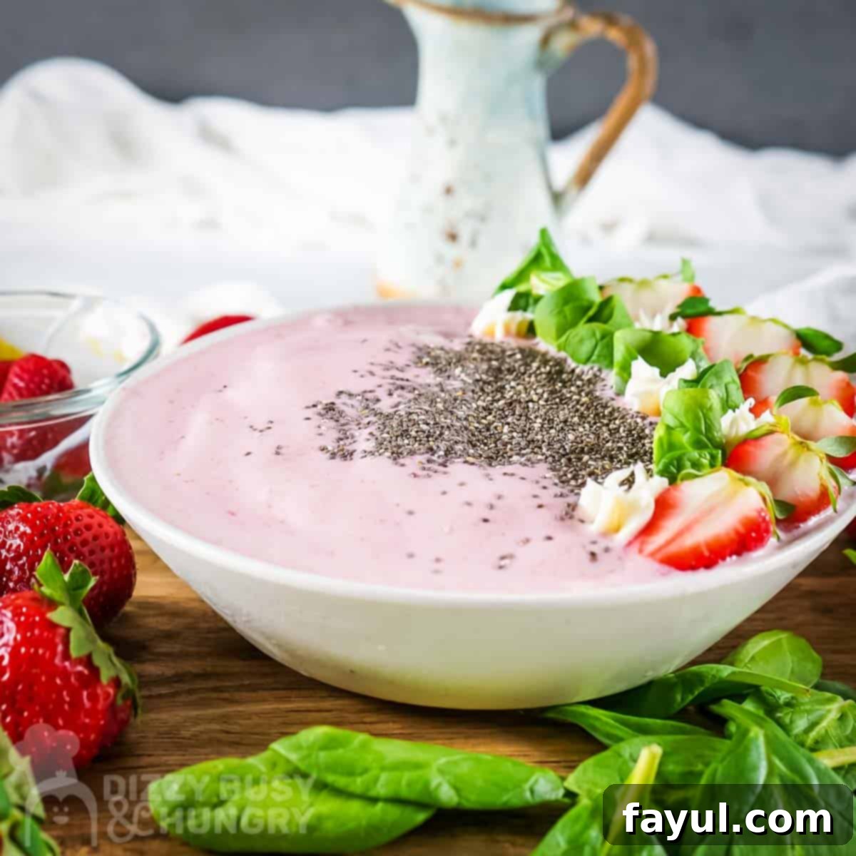 Side view of smoothie bowl garnished with flax seeds, mint, and sliced strawberries on a wooden surface with more mint and strawberries on the side.