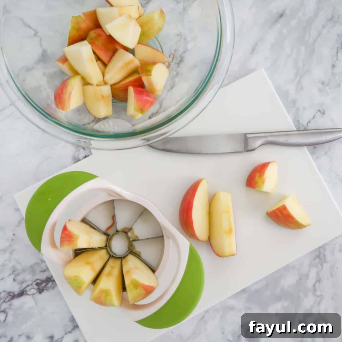 Overhead view of process shot 1 - using an apple wedge to slice apples on a white cutting board.