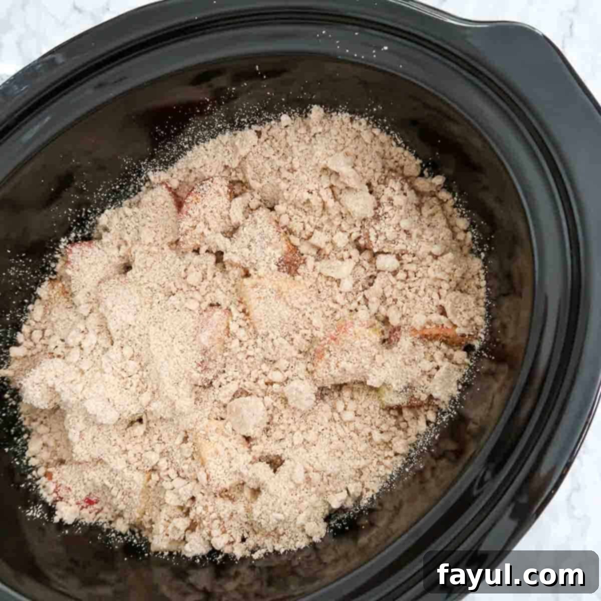 Overhead view of process shot 9 - adding crumble topping to apple mixture in crock pot.