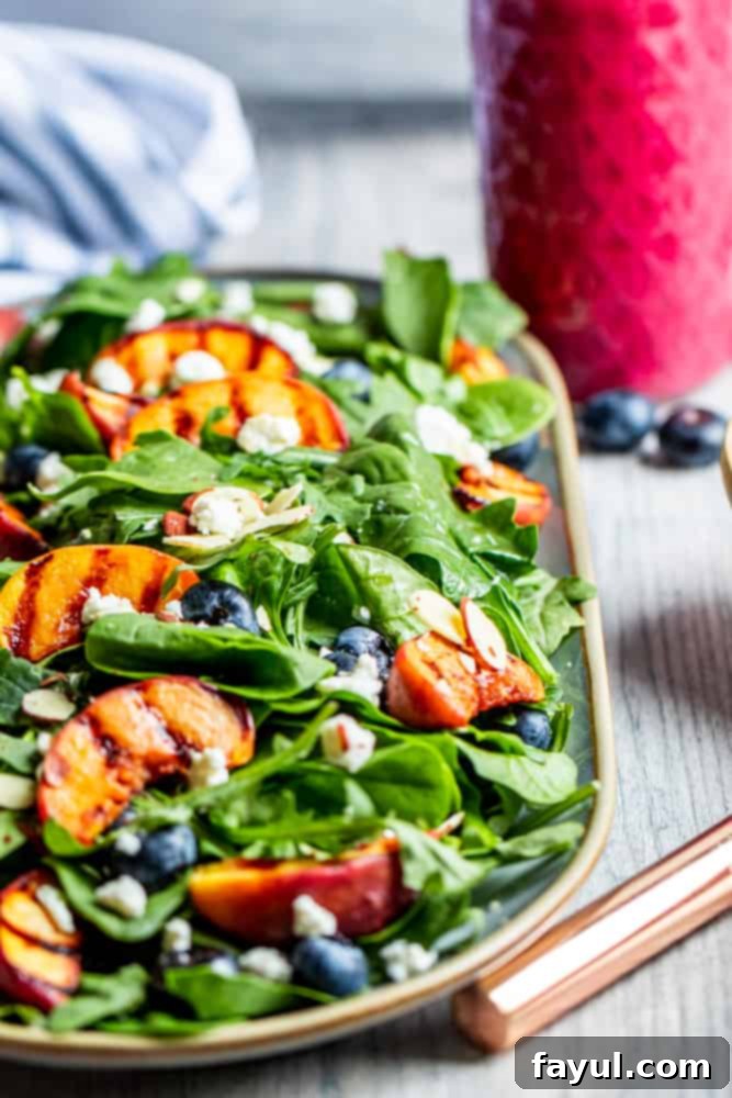 Grilled peach salad on a platter with pink dressing in the background.