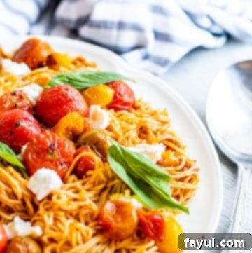Beautifully plated Red Pesto Pasta on a white dish on a white table, with a silver spoon poised next to it for serving.