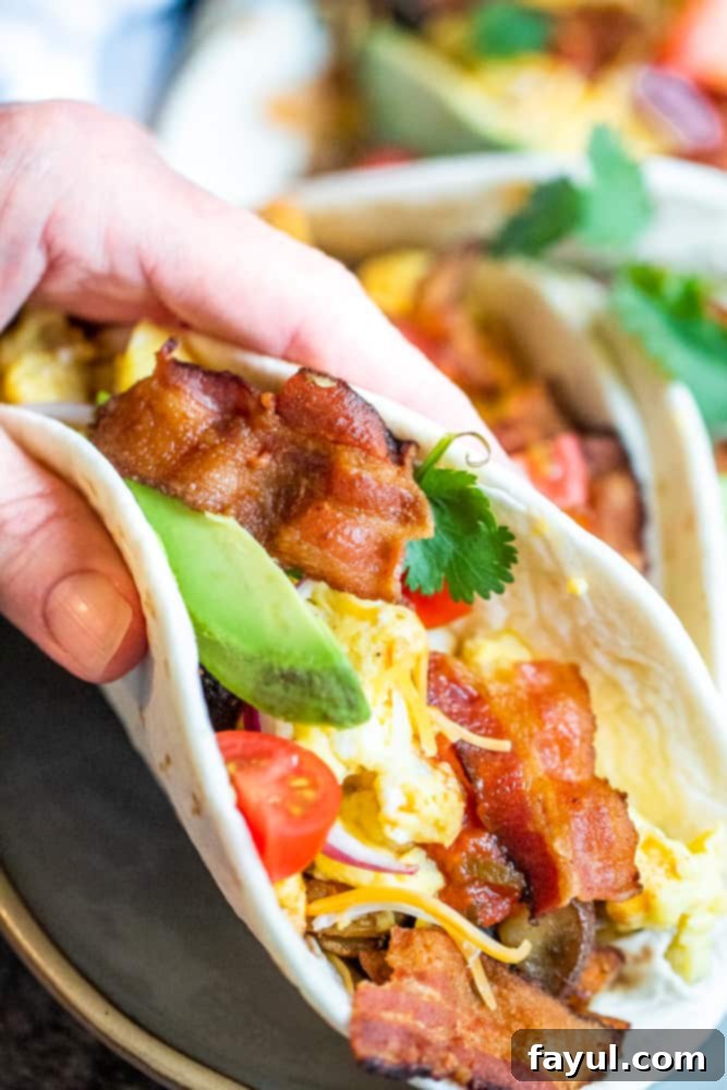 A hand holding a delicious breakfast taco, positioned closely to the camera lens, showcasing its inviting texture and fillings.