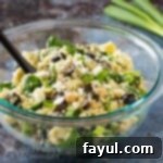 Side view of finished Quinoa Chickpea Salad in a clear bowl with a black spoon in front of scallions.