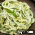 Close up shot of zucchini noodles in avocado sauce garnished with basil in a brown speckled bowl.