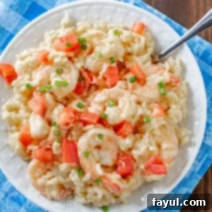 Overhead shot of creamy shrimp and rice garnished with chives on a white plate with a fork and a blue cloth on the side.