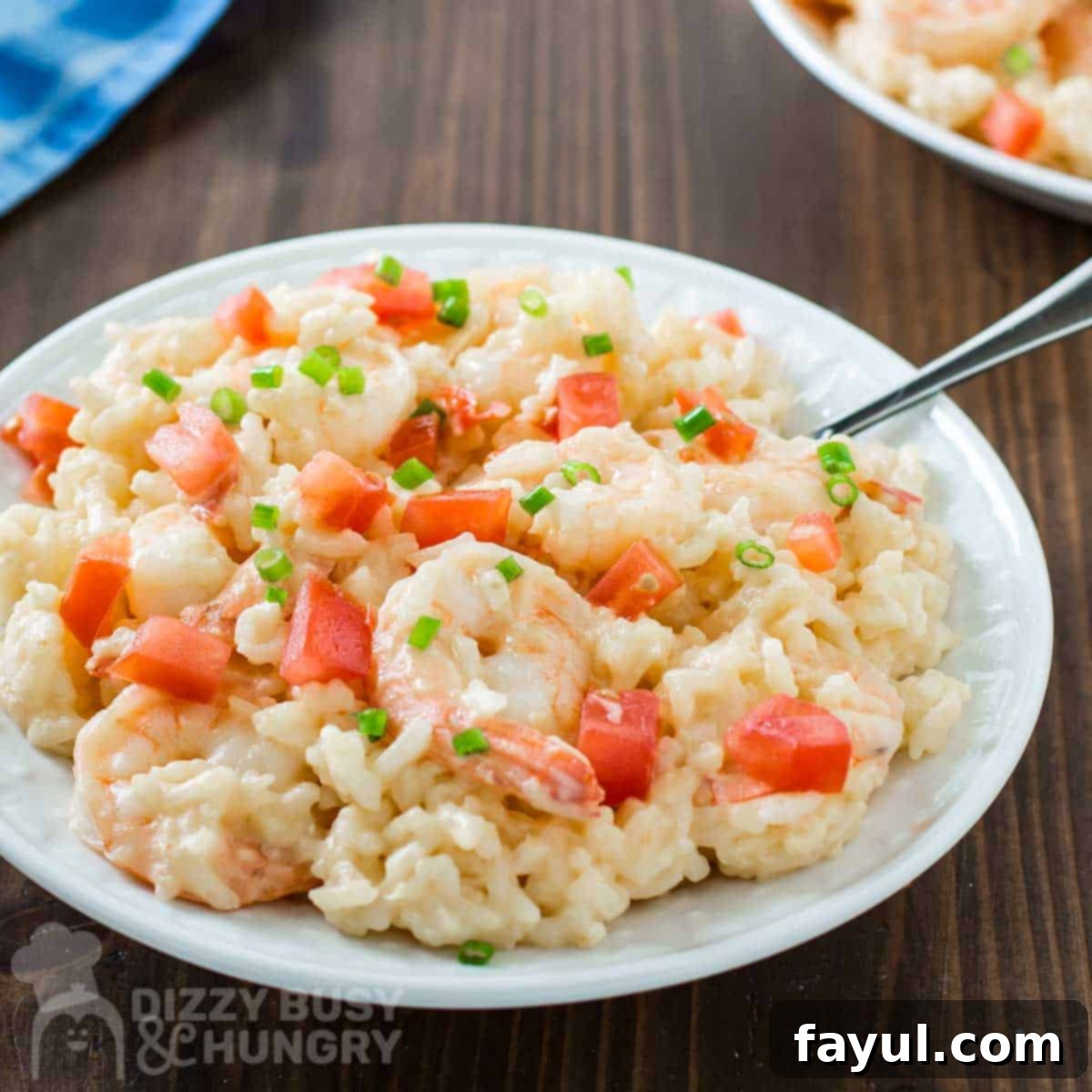Side shot of creamy shrimp and rice garnished with chives on a white plate with a fork and a blue cloth on the side.