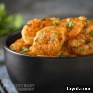 Side shot of shrimp garnished with fresh parsley in a black bowl with more herbs on the side.