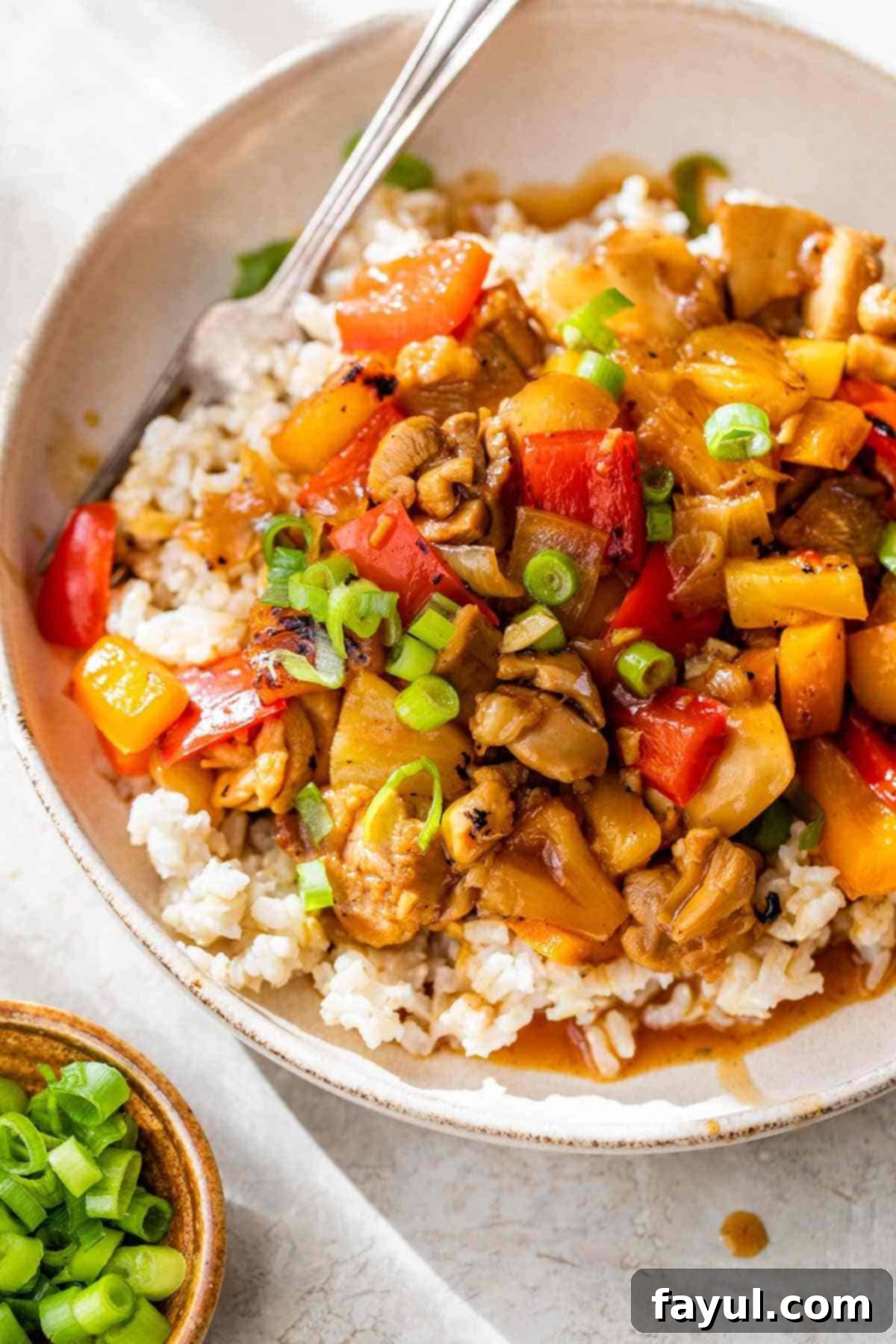 Bowl of cooked chicken, rice, red and yellow peppers, and scallions covered in a light brown sauce.