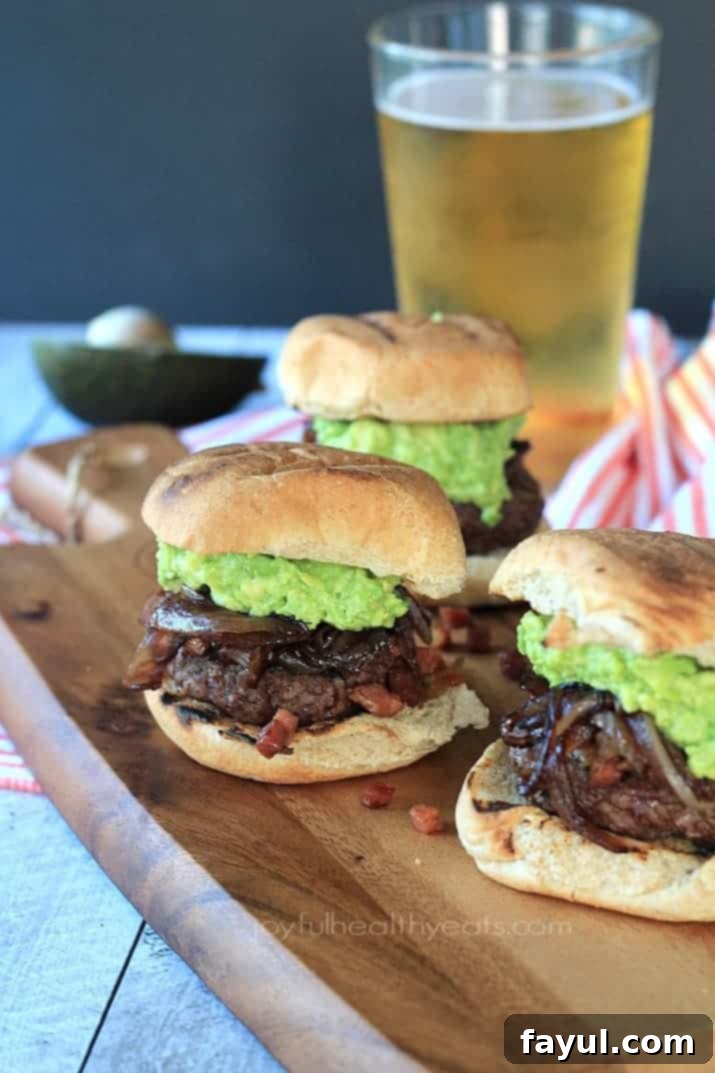 Three small burgers on buns with creamy avocado, caramelized onions, and pancetta.