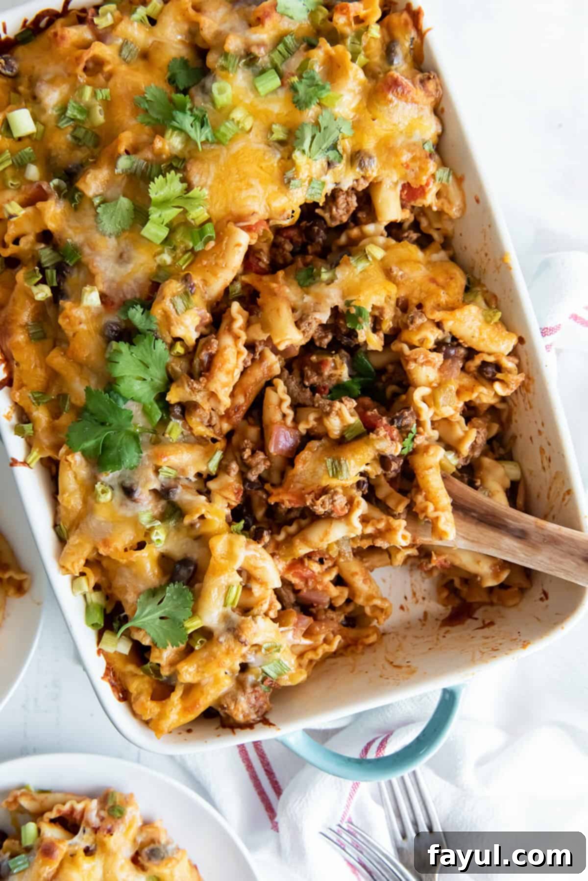 White casserole dish containing Taco Pasta Bake with ground beef and bean mixture, pasta, and cilantro in a taco inspired brown sauce.