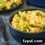 Side close up shot of Mac and cheese with broccoli in a black bowl on a blue speckled surface with a black fork on the side.