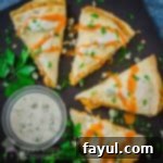 Overhead view of a cut quesadilla drizzled with buffalo sauce and blue cheese garnished with herbs on a black plate with a side of ranch in a white bowl.