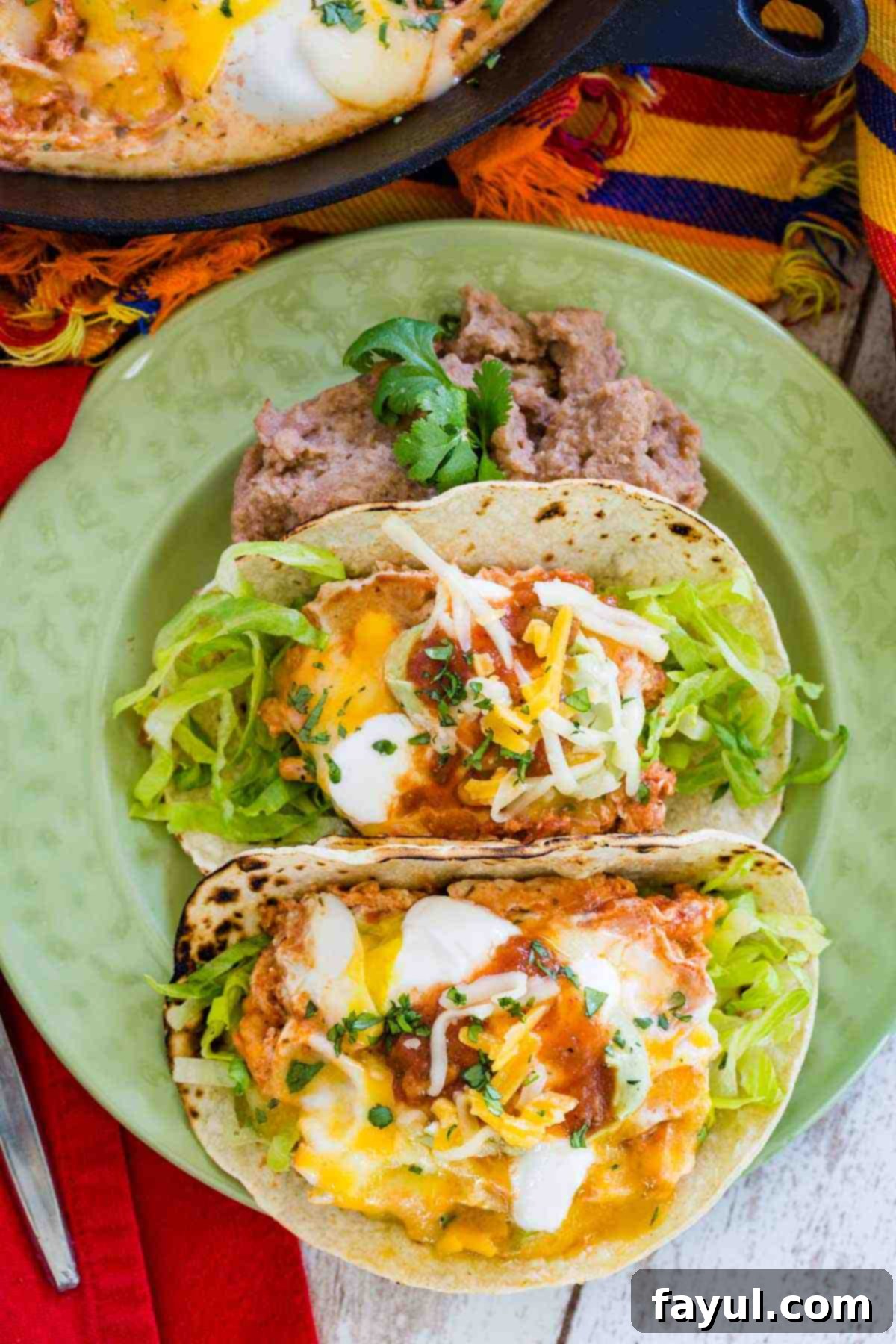 A green plate with two tacos stuffed with eggs, salsa, and cheese drizzled with salsa.