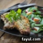 Side view of blue cheese encrusted pork chops garnished with herbs with a side of spinach sprinkled with apples and cranberries on a black plate.