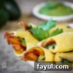 Side shot of taquitos layered on a white plate garnished with cilantro with a bowl of guacamole in the background.