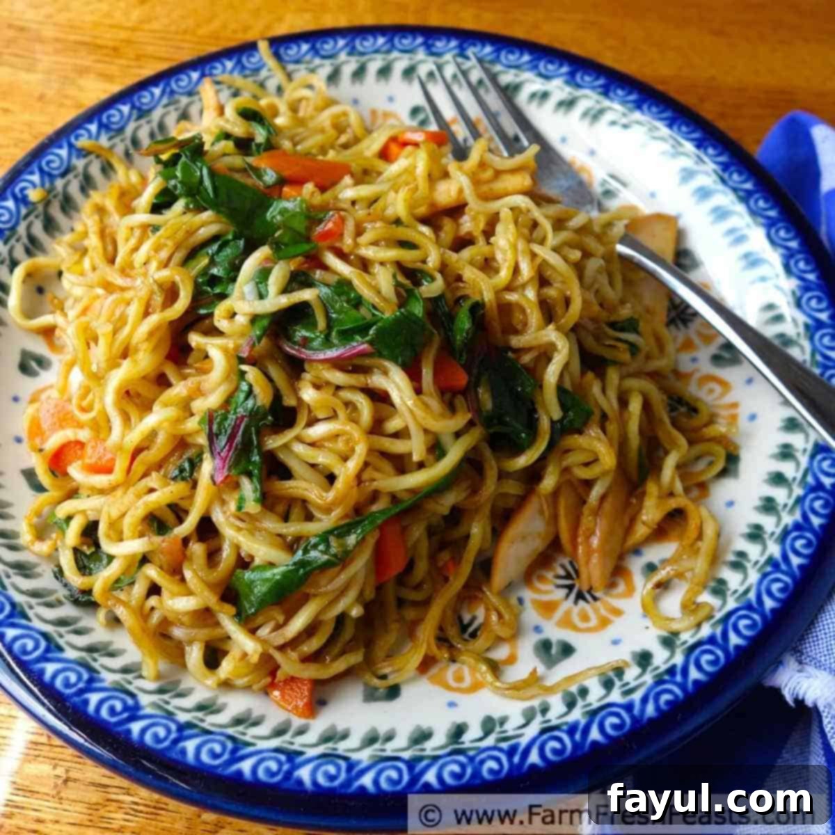 White dish with blue border filled with stir fry noddles, ham, and vegetables in a light brown sauce.