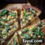 Side angled shot of multiple slices of steak pizza garnished with arugula on a wooden cutting board.