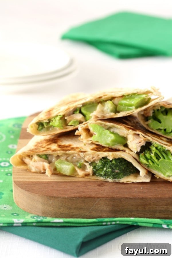 Cutting board on green table cloth with four Chicken And Broccoli Alfredo Quesadillas.