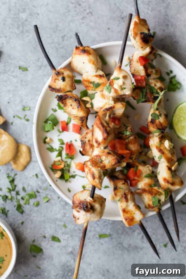 A while bowl with skewers of grilled chicken sprinkled with green parsley and chopped red peppers.