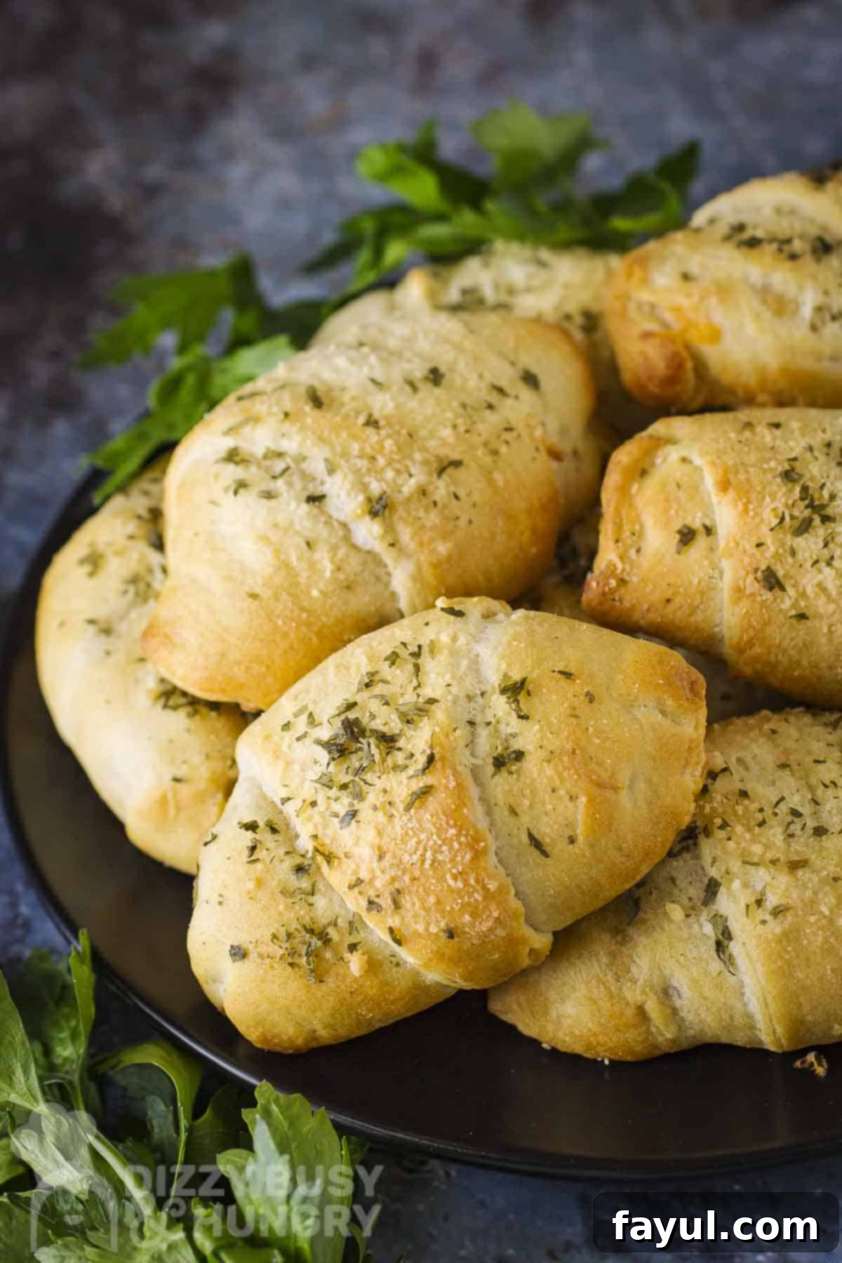 Side angled shot of golden brown zucchini cheese bites stacked on a black plate with fresh herbs on the side.