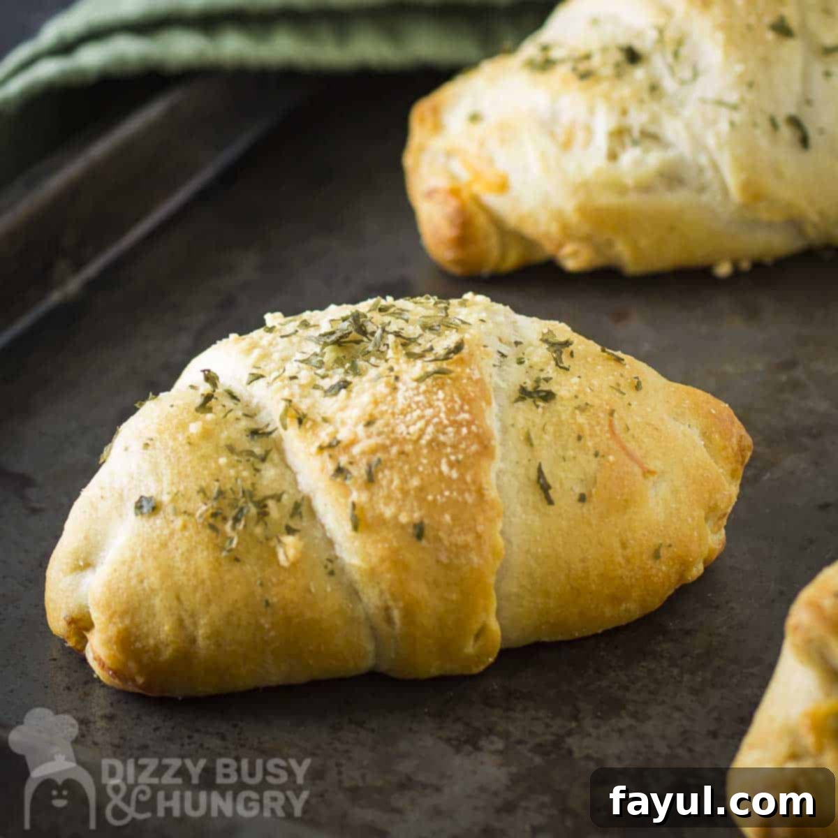 Side close up shot of cheesy zucchini bites on a baking sheet with a sage green cloth on the side, showing their golden crust and melted cheese.