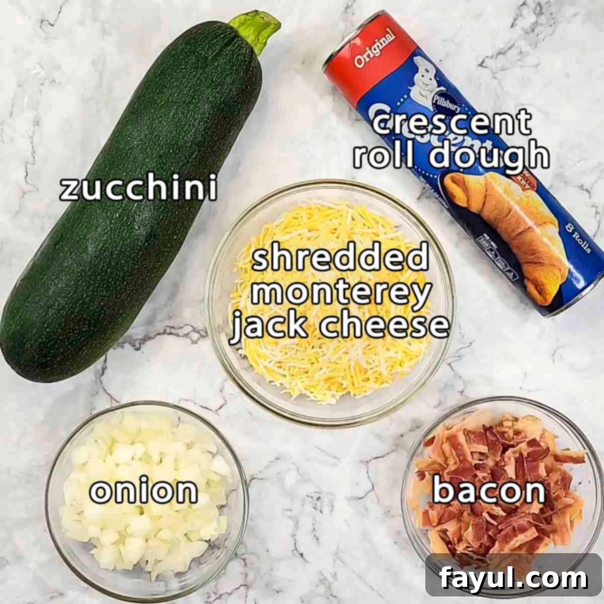 Overhead shot of all the key ingredients needed for zucchini cheese bites including fresh zucchini, crescent roll dough, shredded monterey jack cheese, diced onion, and cooked bacon.