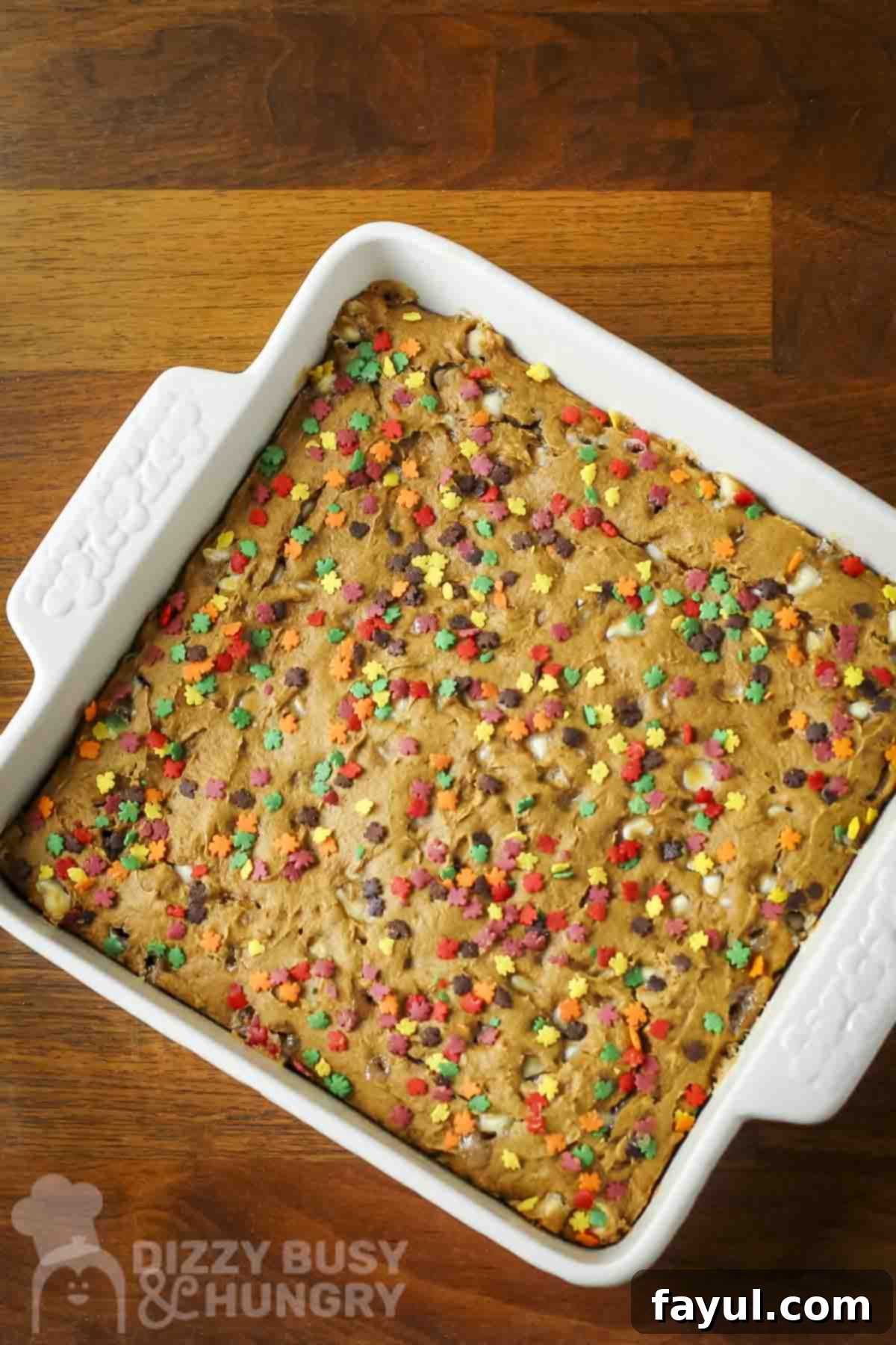 Overhead shot of spice cake with fall-themed sprinkles in a white square baking dish on a wooden surface.