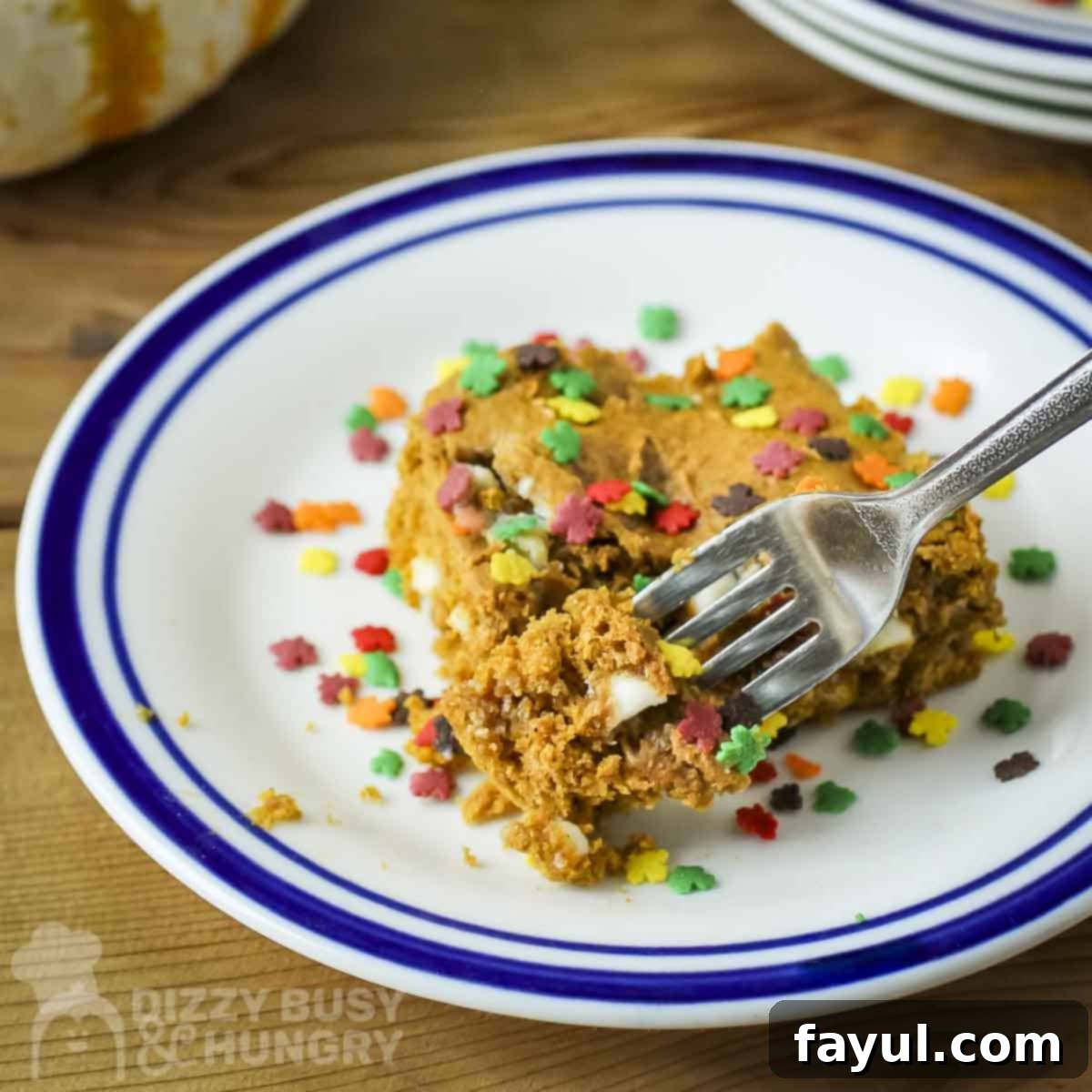 Side angled shot of a slice of spice cake with fall-themed sprinkles on a white and blue plate with a fork picking up a piece.