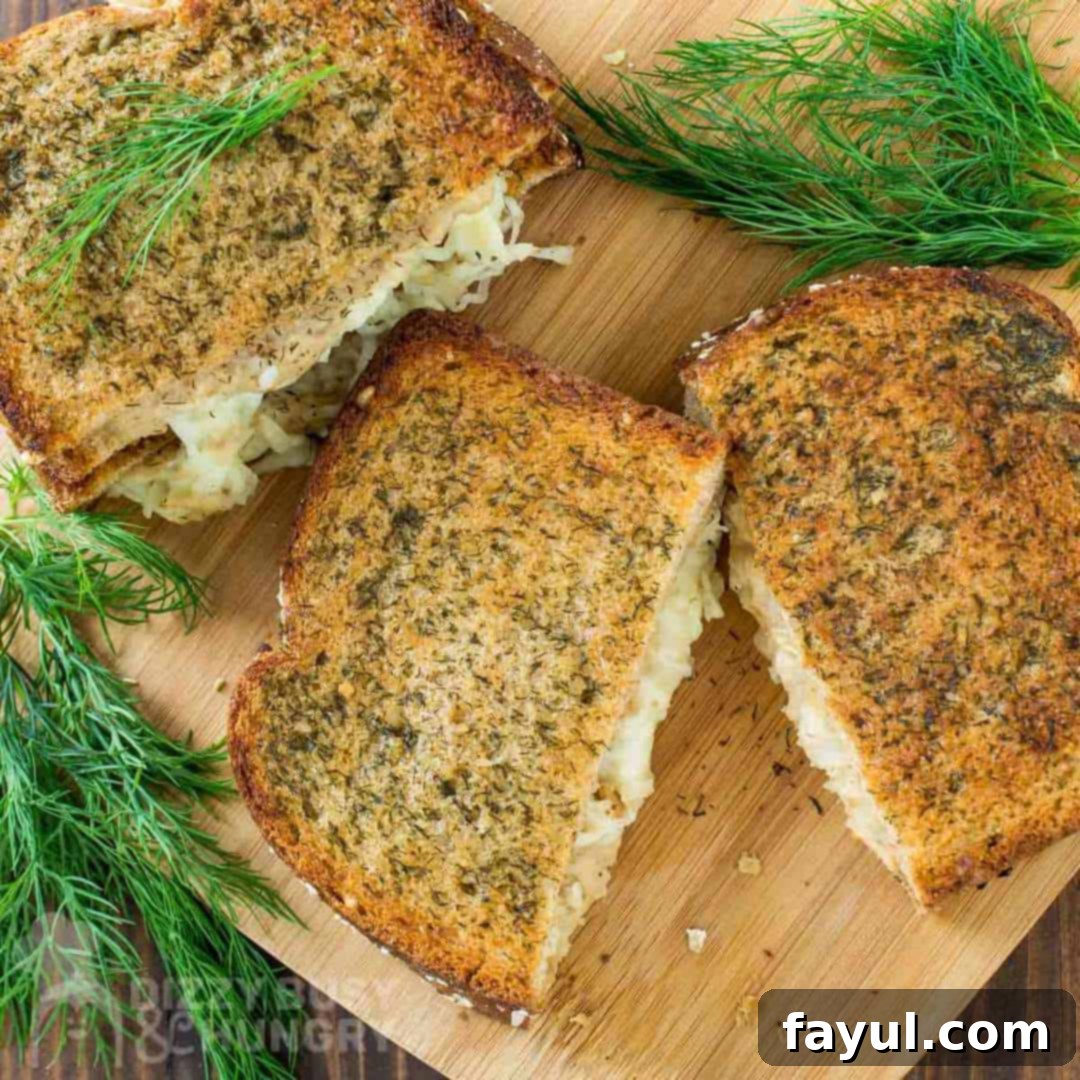 Overhead view of a gourmet grilled cheese sandwich cut in half, showcasing the melty cheese, salmon, and apple filling on a wooden cutting board, garnished with fresh dill.
