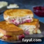 Side view of three stacked halves of brie grilled cheese with cranberry sauce and sliced turkey on a blue background.