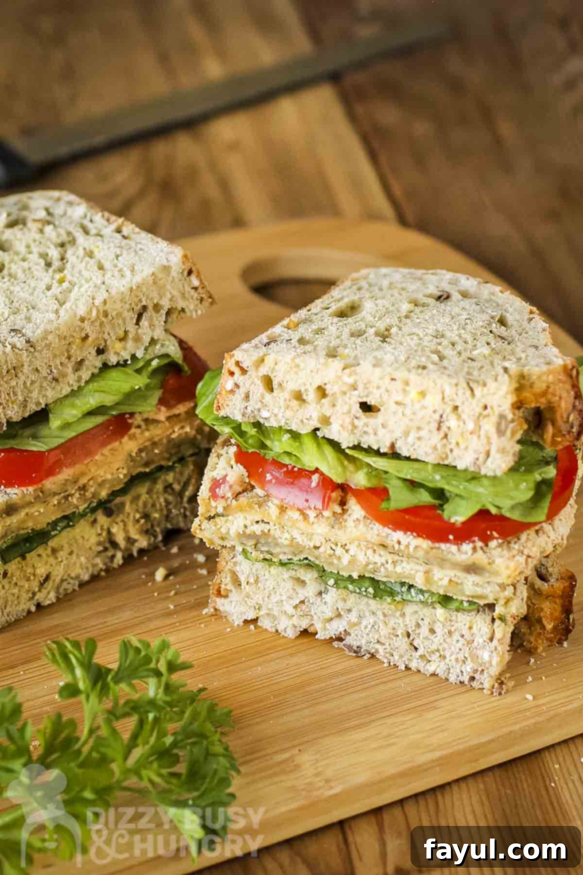 Side shot of a milanese sandwich cut in half on a wooden cutting board with herbs on the side, highlighting the crispy eggplant.