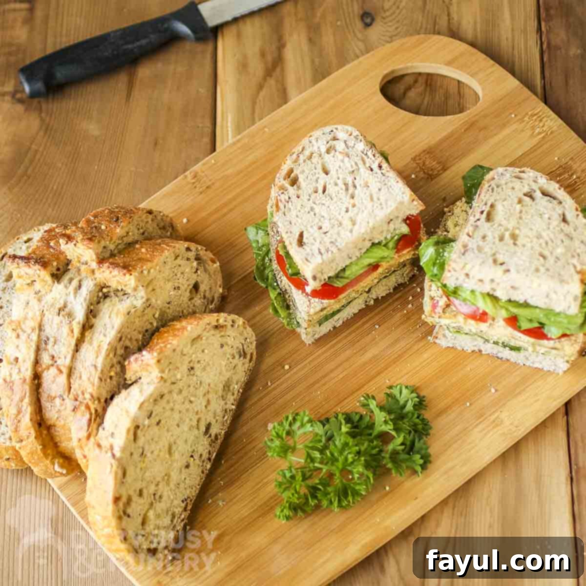 Side shot of a milanese sandwich cut in half on a wooden cutting board with sliced bread and fresh herbs on the side, ready to be served.