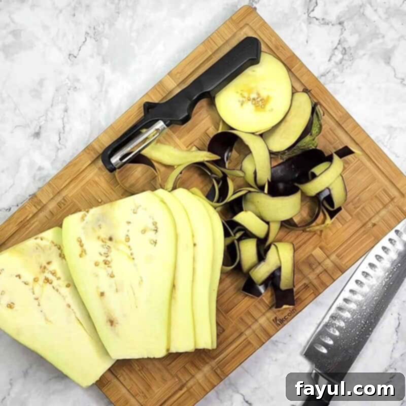 Overhead view of process shot 1 - remove the ends from the eggplant and use a peeler to remove the skin. Slice it lengthwise into sections about ¼ inch thick.