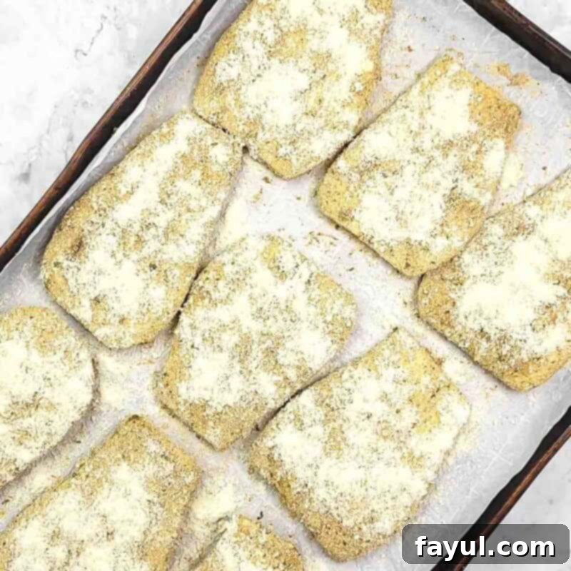 Overhead view of process shot 5 - place the eggplant on a baking sheet lined with parchment paper and bake 8 minutes. Then turn the slices over and sprinkle with parmesan cheese. Bake for another 5 minutes.