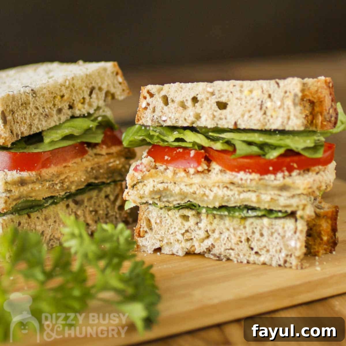 Side shot of a baked eggplant sandwich cut in half on a wooden cutting board with fresh herbs on the side, showing the delicious layers.
