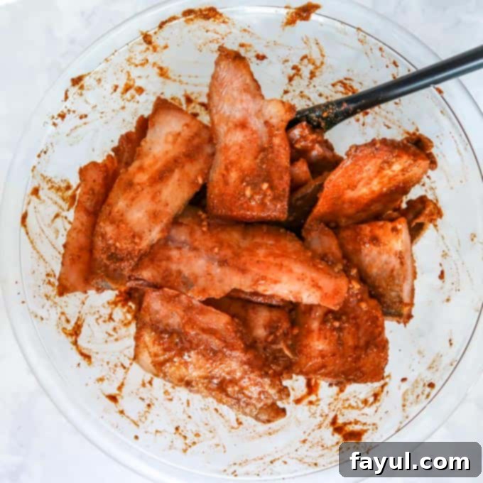 Close up view of tilapia coated with orange-red marinade in a clear bowl.