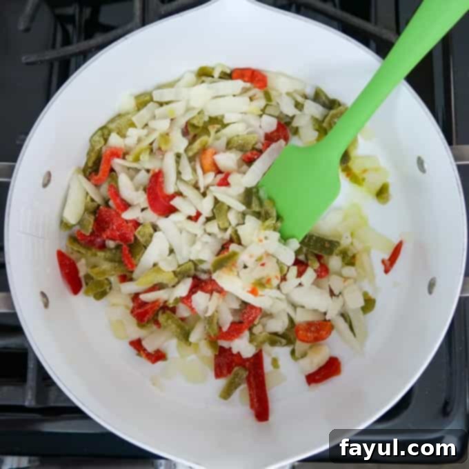Overhead shot of olive oil, peppers, and onions in a white sauce pan on the stove.