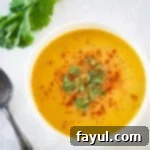 Overhead shot of butternut squash and carrot soup garnished with herbs and spices in a white bowl with herbs and a spoon on the side.