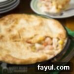 Side shot of seafood pot pie with a slice taken out on a green potholder with plates in the background.