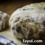 Side view of whole loaf of olive bread on a wooden cutting board with a butter knife on the side.