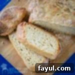 Overhead shot of half of the bread loaf with some slices on a wooden cutting board with a blue background.