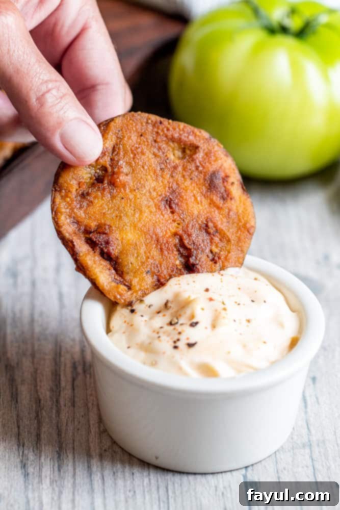 Hand dipping fried green tomato in a white bowl of hot mayo.