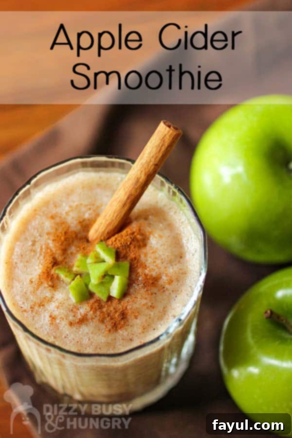 Close up shot of a fall-themed apple smoothie with a sprinkle of cinnamon and a cinnamon stick on top, served in a clear glass, placed beside two fresh granny smith apples.