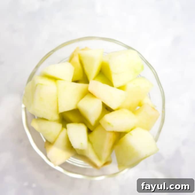 Overhead view of meticulously chopped and peeled apples resting in a clear bowl on a pristine white surface, indicating they are ready for the next step of blending.