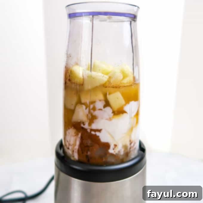 Side view of all the measured ingredients for the apple smoothie mixed together inside a blender cup, ready for the blending process to begin.