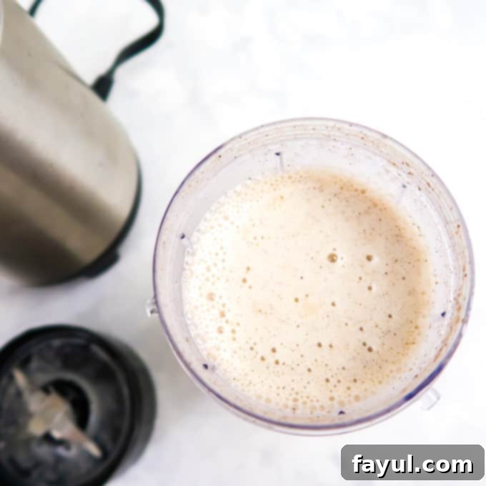Overhead view of a perfectly well-blended apple smoothie in a clear blender cup, with the blender base visible on the side, indicating it's ready to be served.