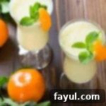 Overhead shot of two glasses of pineapple orange smoothie garnished with orange slices and fresh mint sprigs.
